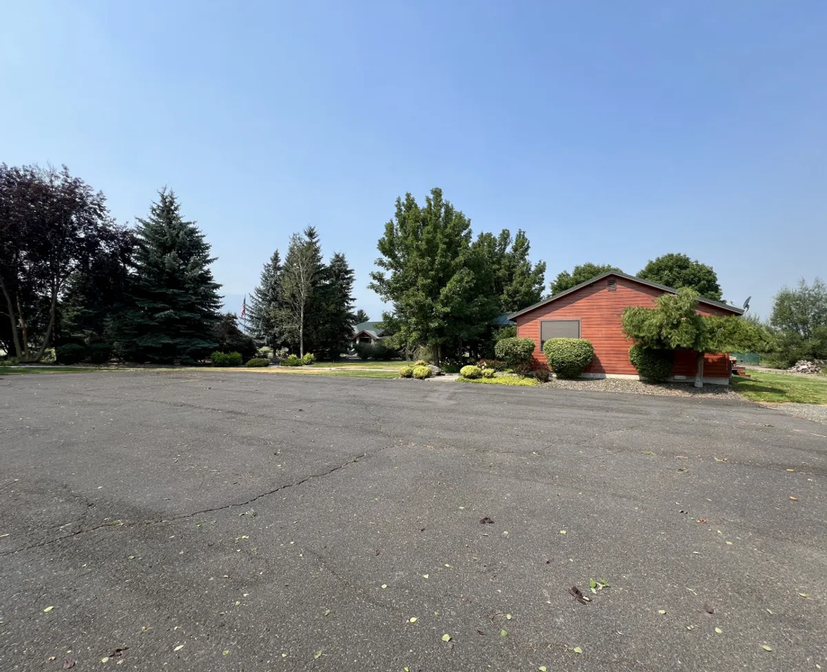 The image shows a red wooden house nestled among vibrant green trees and a well-maintained lawn, evoking tranquility and a connection to nature. The setting invites guests to imagine serene moments before or after their golf outings.