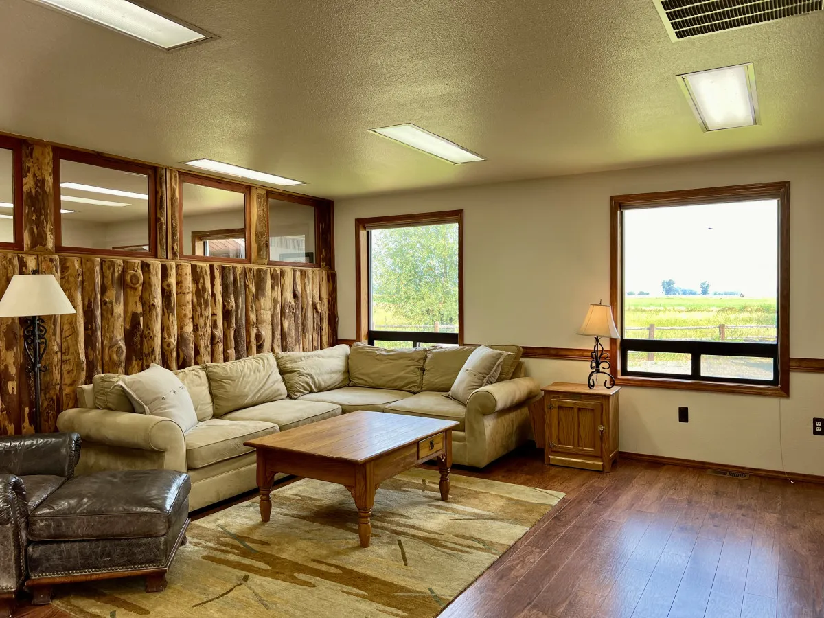 A spacious lounge with a large sectional sofa, wooden coffee table, an armchair, and wide windows letting in plenty of natural light. The arrangement is ideal for group conversation, relaxation, or family gatherings.