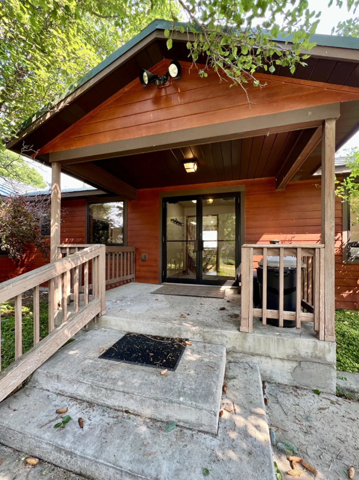 This exterior perspective highlights the home's inviting front porch framed by double glass doors, wooden railings, and seasonal decorations. Thoughtful landscaping surrounds the porch, where guests may gather for coffee, conversation, or simply to take in the fresh country air.