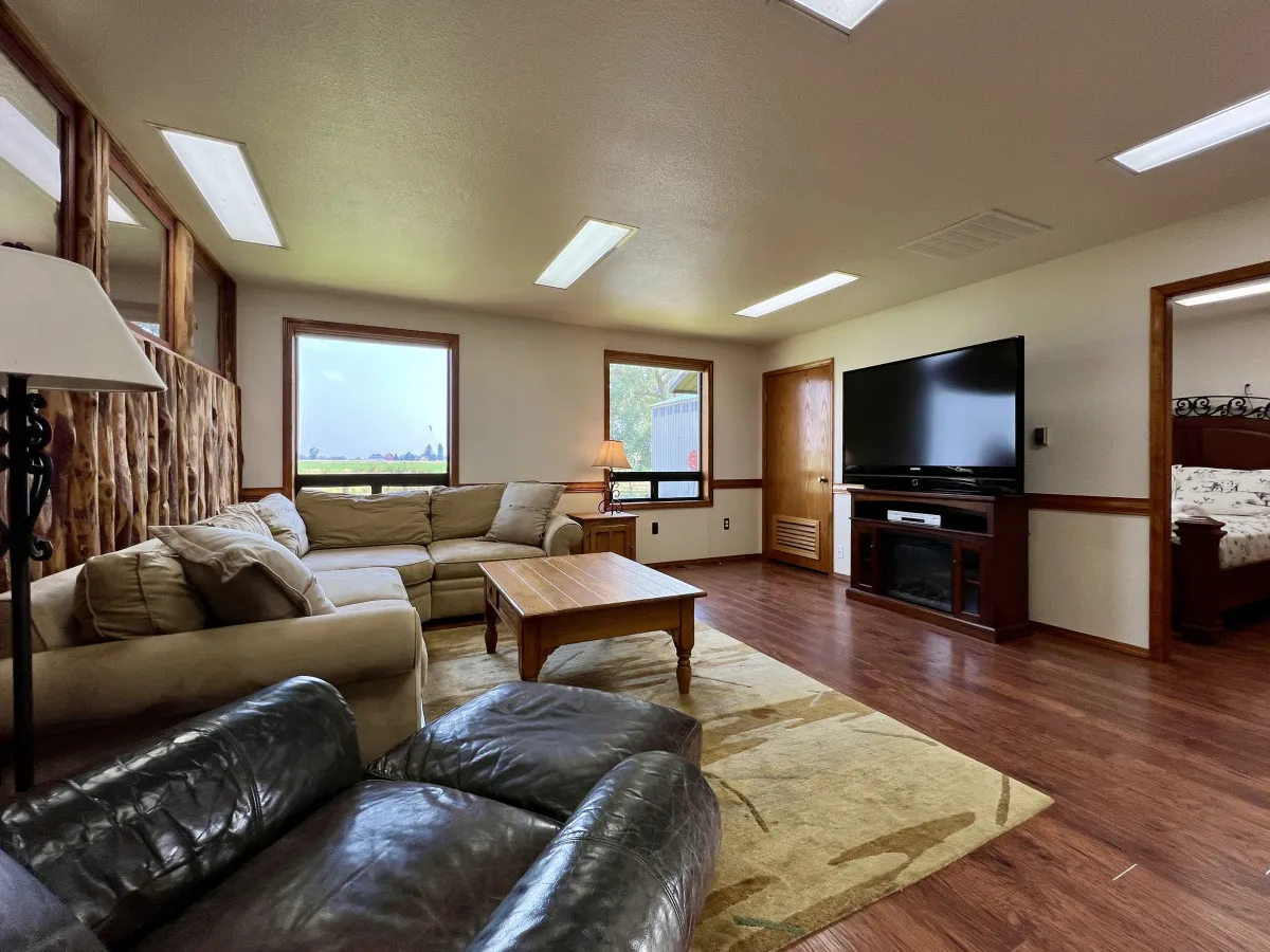 A cozy living room with a plush sofa arranged around a large coffee table, windows offering glimpses of the mountains, and a TV for movie nights. The room is bathed in natural light and invites relaxation and socializing.