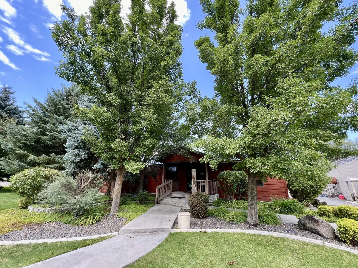 The image captures the inviting front porch of the property, framed by mature trees and a beautifully landscaped garden. The scene suggests opportunities for relaxing with morning coffee or gathering with friends after a day on the golf course.