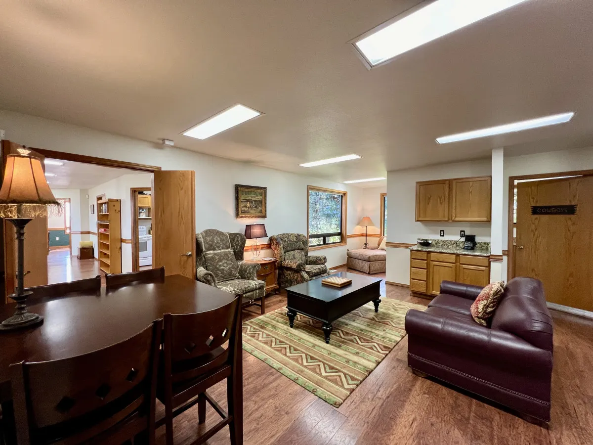 The image showcases a welcoming open-concept living space featuring a plush, comfortable seating area, a spacious dining table perfect for gatherings, and a well-equipped kitchenette—inviting guests to relax, share meals, and enjoy quality time together.
