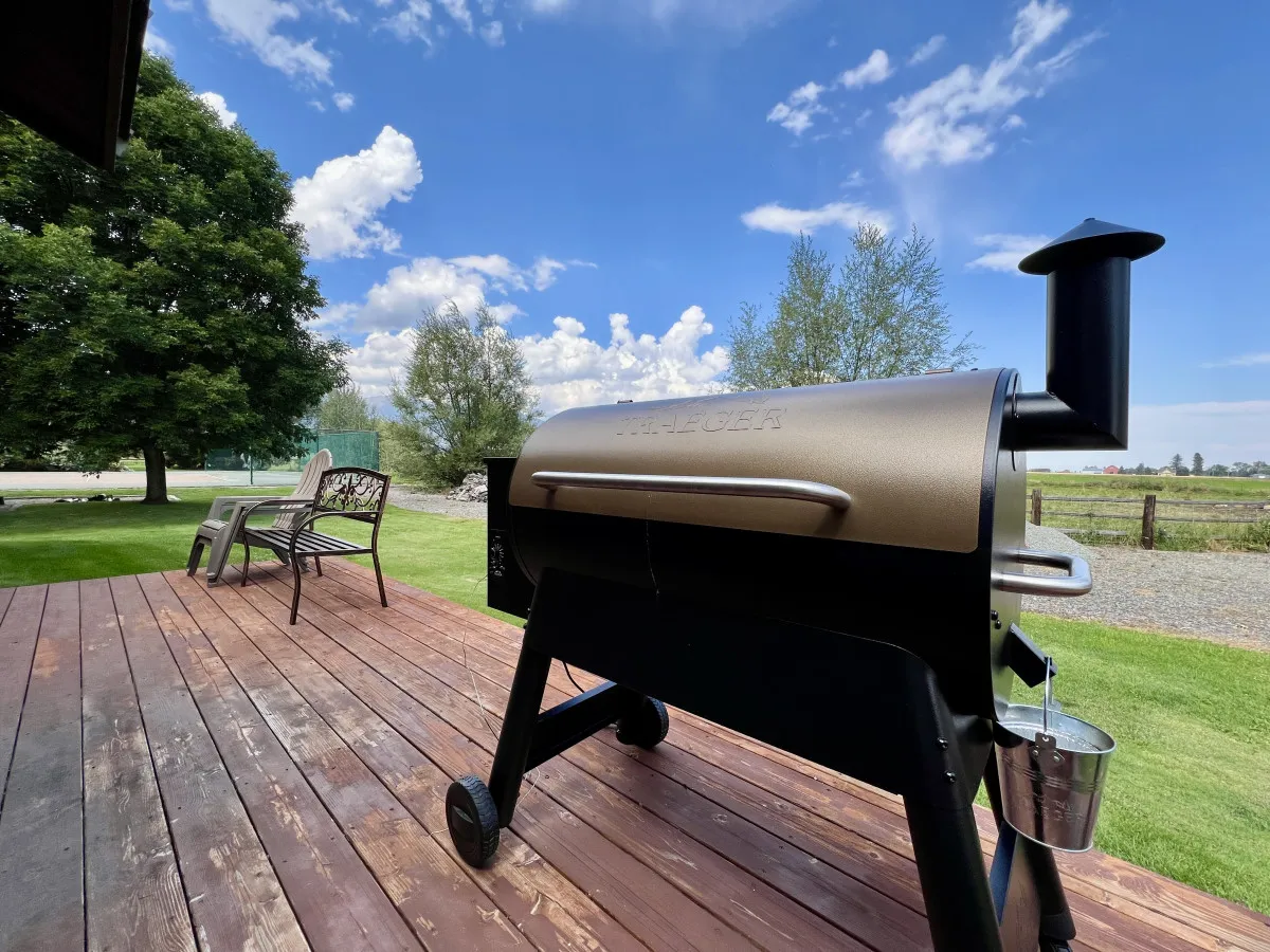 This image presents a wooden back deck equipped with a grill, overlooking a lush green lawn under a clear blue sky. The deck is designed for outdoor dining or gatherings, seamlessly blending relaxation with recreation.