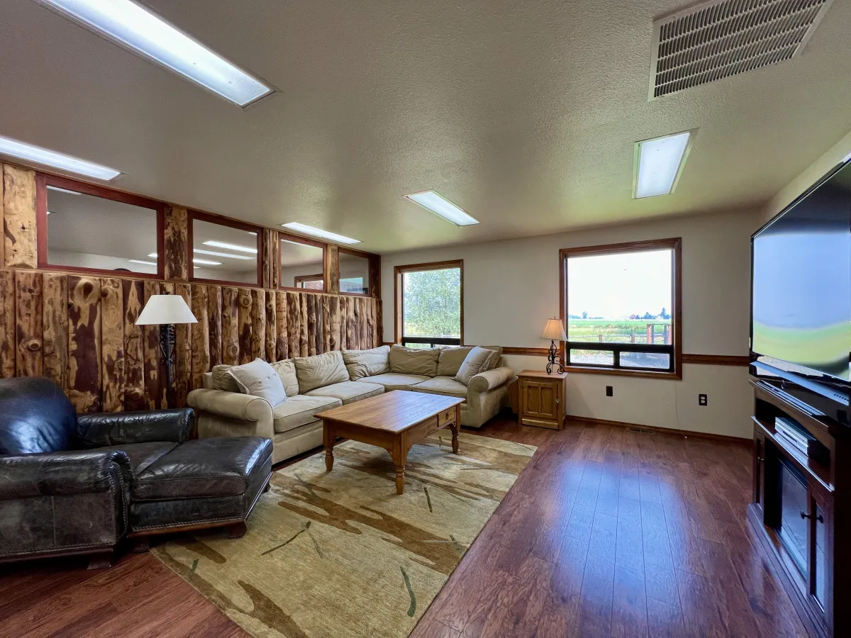 An inviting living area featuring a large sectional sofa, wooden coffee table, lamps, television, and expansive windows. The setup is designed for entertaining guests, family time, or cozy evenings together.