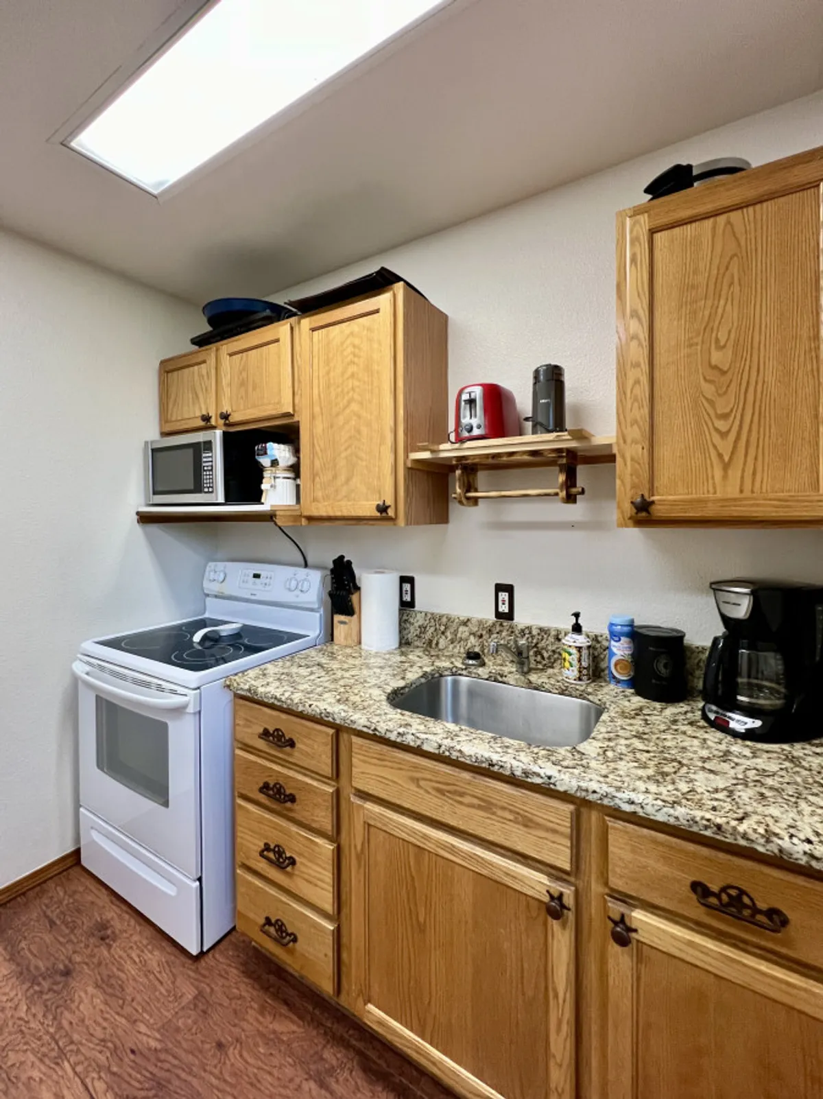 This image showcases a cozy, functional kitchen with granite countertops, wooden cabinets, and modern appliances. The space feels open and practical, ideal for multiple people to cook together or gather while meals are being prepared.