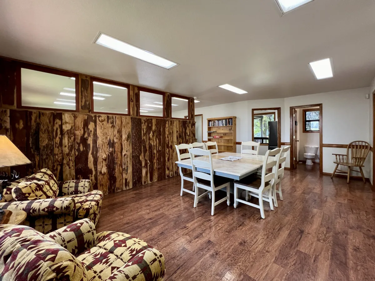 A warm dining room scene with a large dining table, armchair, and rustic wood paneling, creating a cozy environment for family meals, game nights, or late-night snacks.